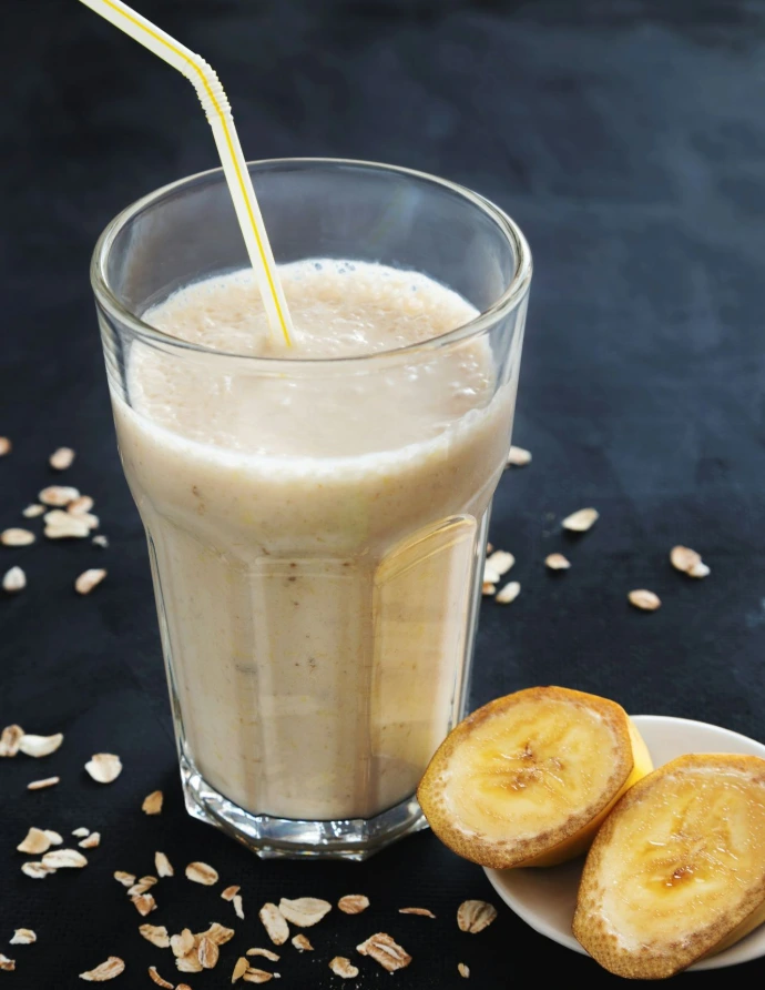 a banana smoothie in a glass next to a plate of sliced bananas